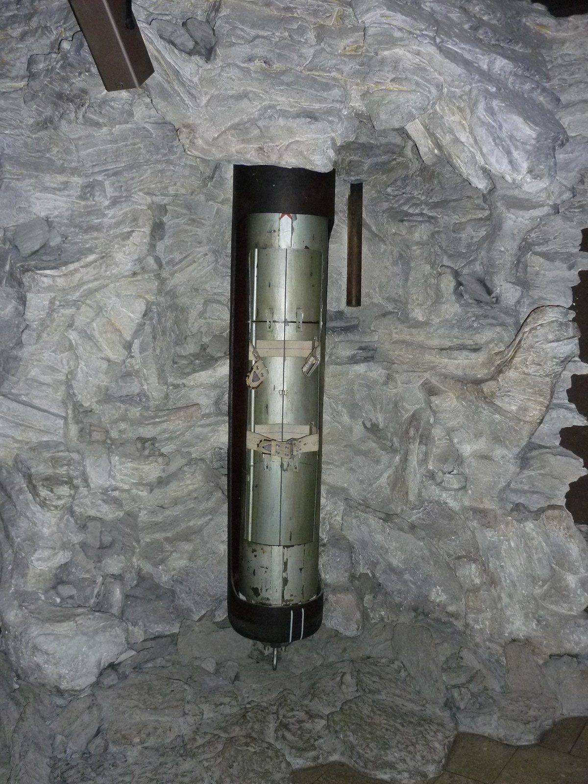 Museumspräsentation der originalen, 2,50 Meter langen und 38,5 Zentimeter schmalen Dahlbuschbombe in einem aufgeschnittenen Bohrrohr vor nachgebildeter Felswand im Deutschen Museum München.
