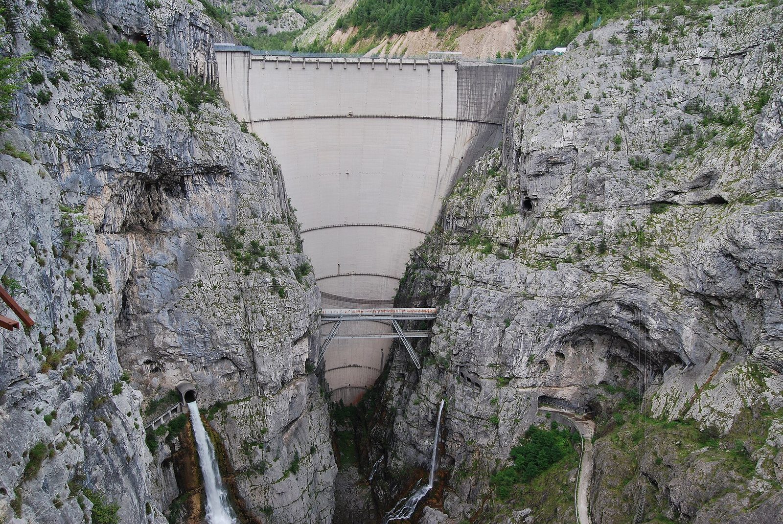 Die doppelt gekrümmte, 261,6 Meter hohe Beton-Bogenstaumauer des Vajont in der engen Kalksteinschlucht zwischen Friaul und Venetien, dahinter der begrünte Schuttberg des Monte-Toc-Bergsturzes, gesehen von Erto.
