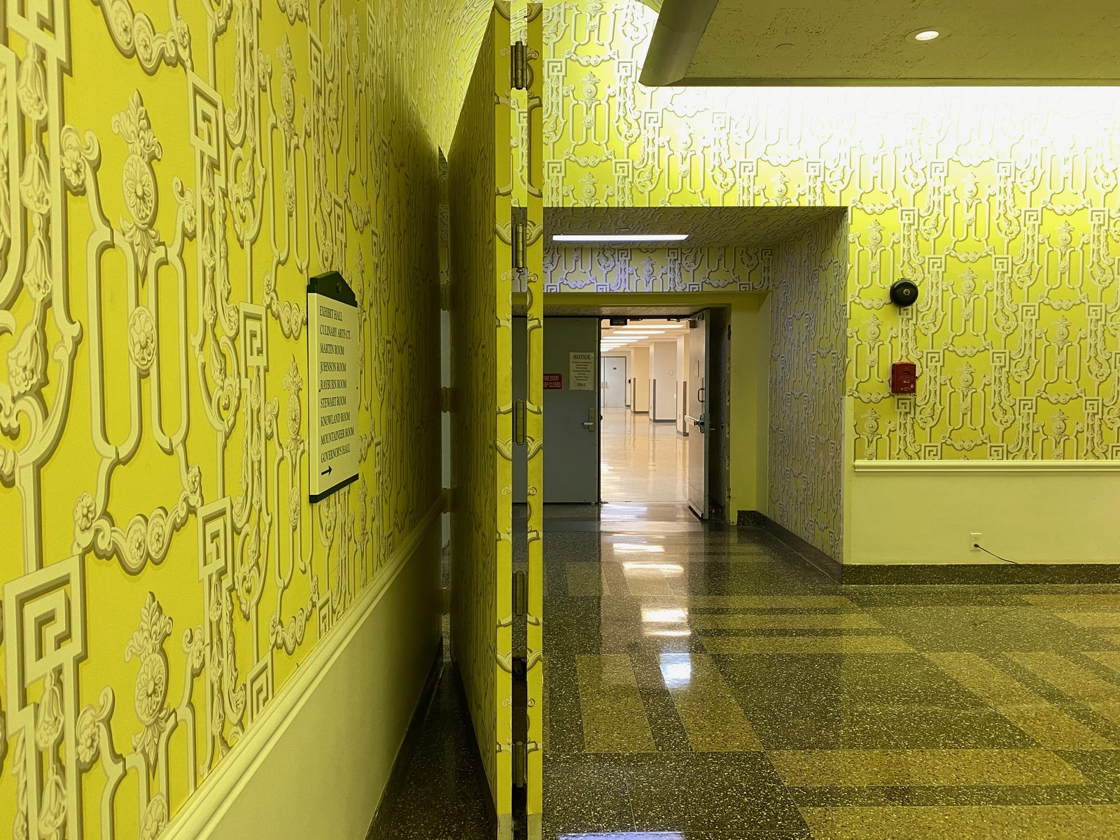Geöffnete, mit gelb-weißer Dorothy-Draper-Tapete versehene Tarnwand (False Wall) im Greenbrier Resort, die den Blick in den dahinterliegenden grauen Bunkerkorridor freigibt.