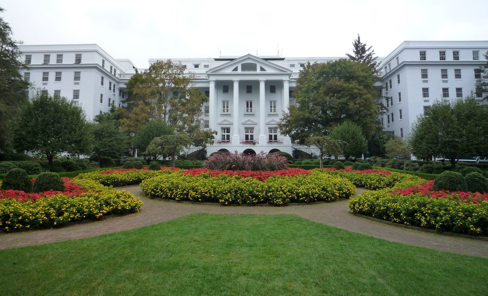 Klassizistischer Nordeingang des weißen Grandhotels The Greenbrier mit Säulenportikus und gepflegten Blumenbeeten im Vordergrund.