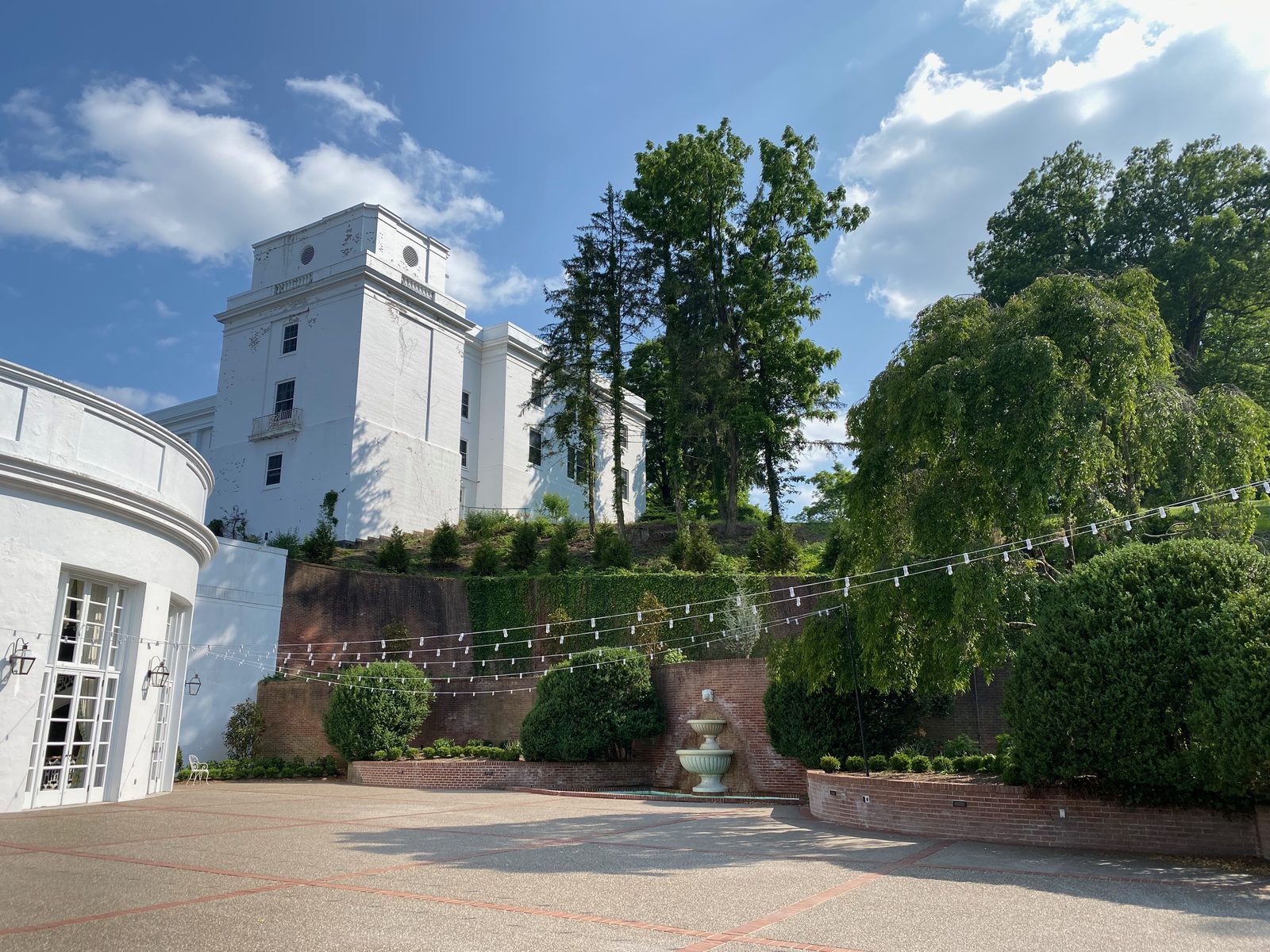 Außenansicht des weißen West Virginia Wing auf der Anhöhe des Greenbrier Resorts mit Ziegelmauer, Brunnen und Terrasse im Vordergrund.
