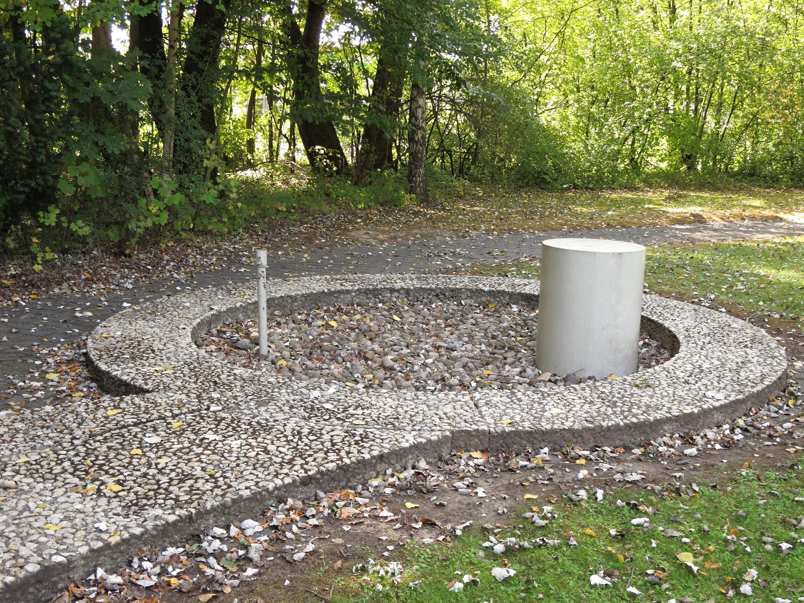 Eingefasste Bohrstelle an der Gedenkstätte Lengede: Links ragt das dünne Stahlrohr der Such- und Versorgungsbohrung (58 mm Durchmesser laut Denkmaltafel, 42 mm laut NDR-Dossier) aus dem Kiesbett, rechts der Rohrstumpf der Rettungsbohrung (480 mm laut Denkmaltafel, 406 mm Innendurchmesser der Verrohrung) zum „Alten Mann“.