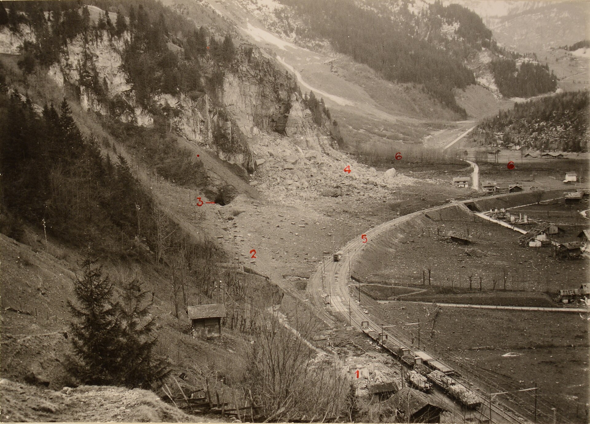 Polizeifoto vom 29. Dezember 1947 mit nummerierten Markierungen: Schutthang unter der Fluh, Standort des zerstörten Stationsgebäudes, verschüttetes Gleis zum Stolleneingang und die Bahnschleife der BLS.