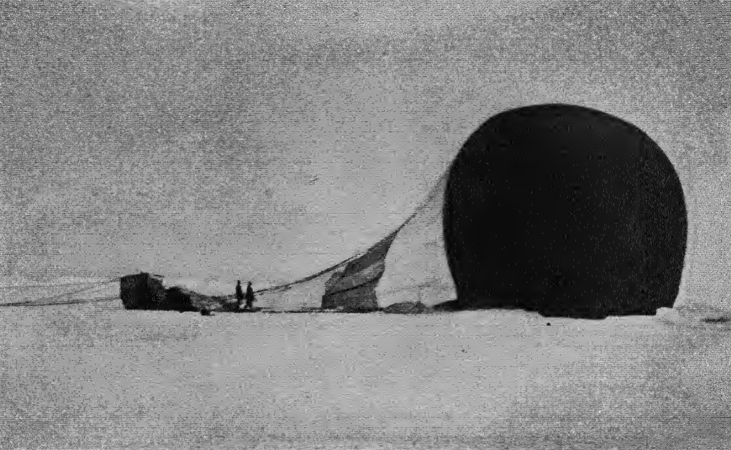 Historisches Schwarzweißfoto: der teilweise entleerte Ballon Örnen liegt auf dem Packeis, links die umgekippte Gondel, daneben zwei kleine Personen